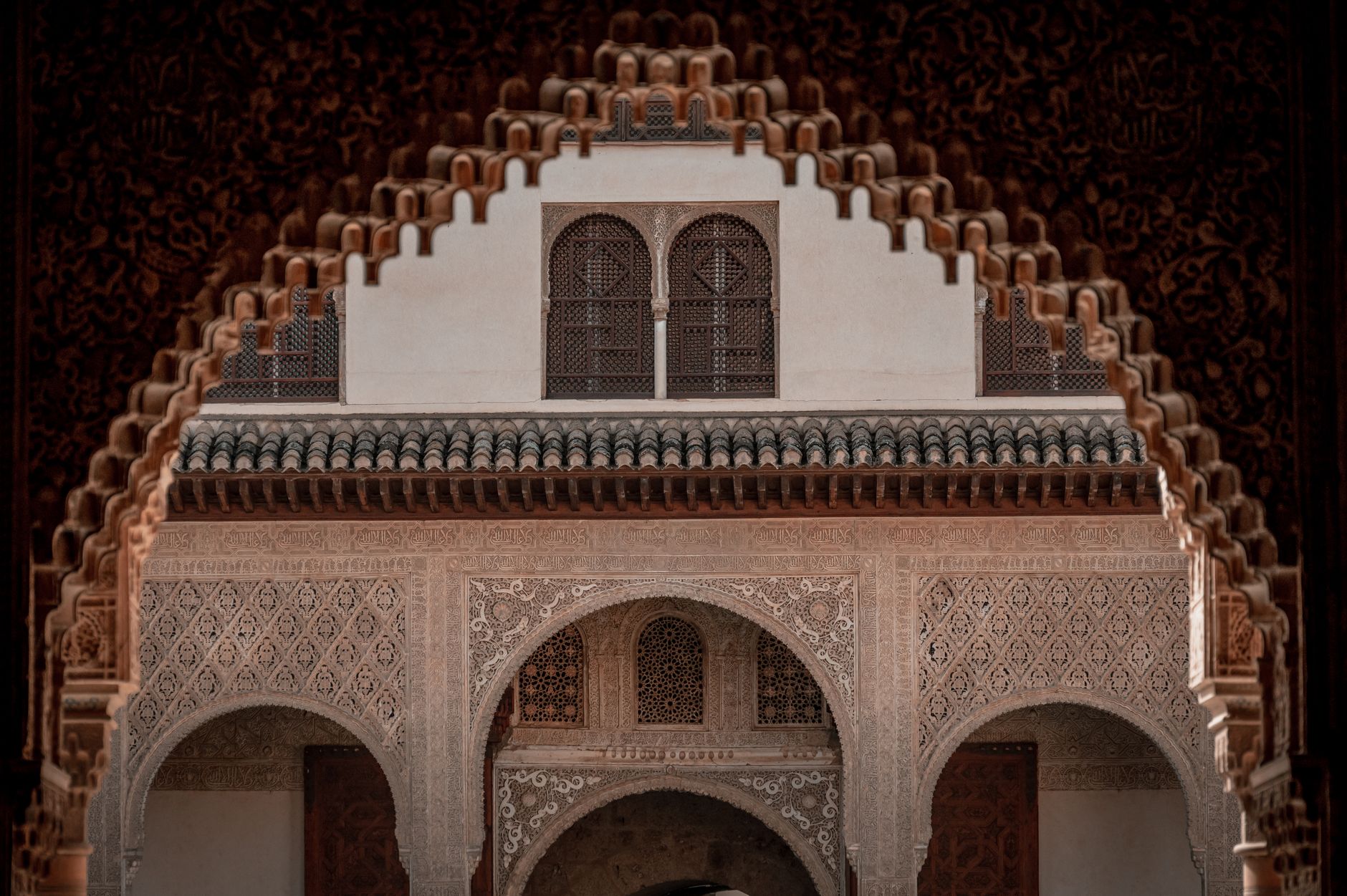 A carved stucco arch in the Alhambra above a wall of geometric zellij tilework