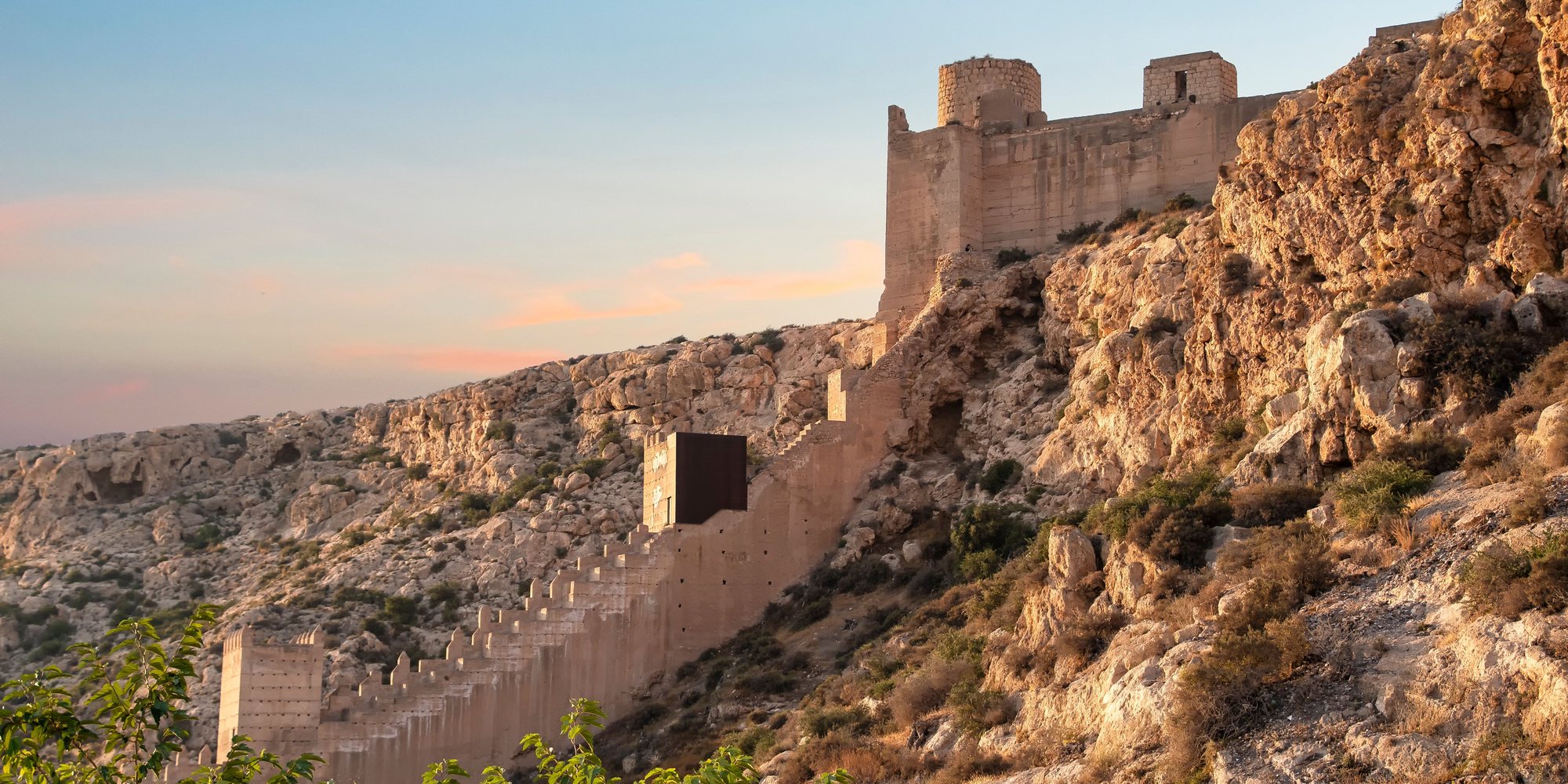 The Moorish walls of the Alcazaba climbing a rocky ridge above Almería at sunset, with a stone tower at the top