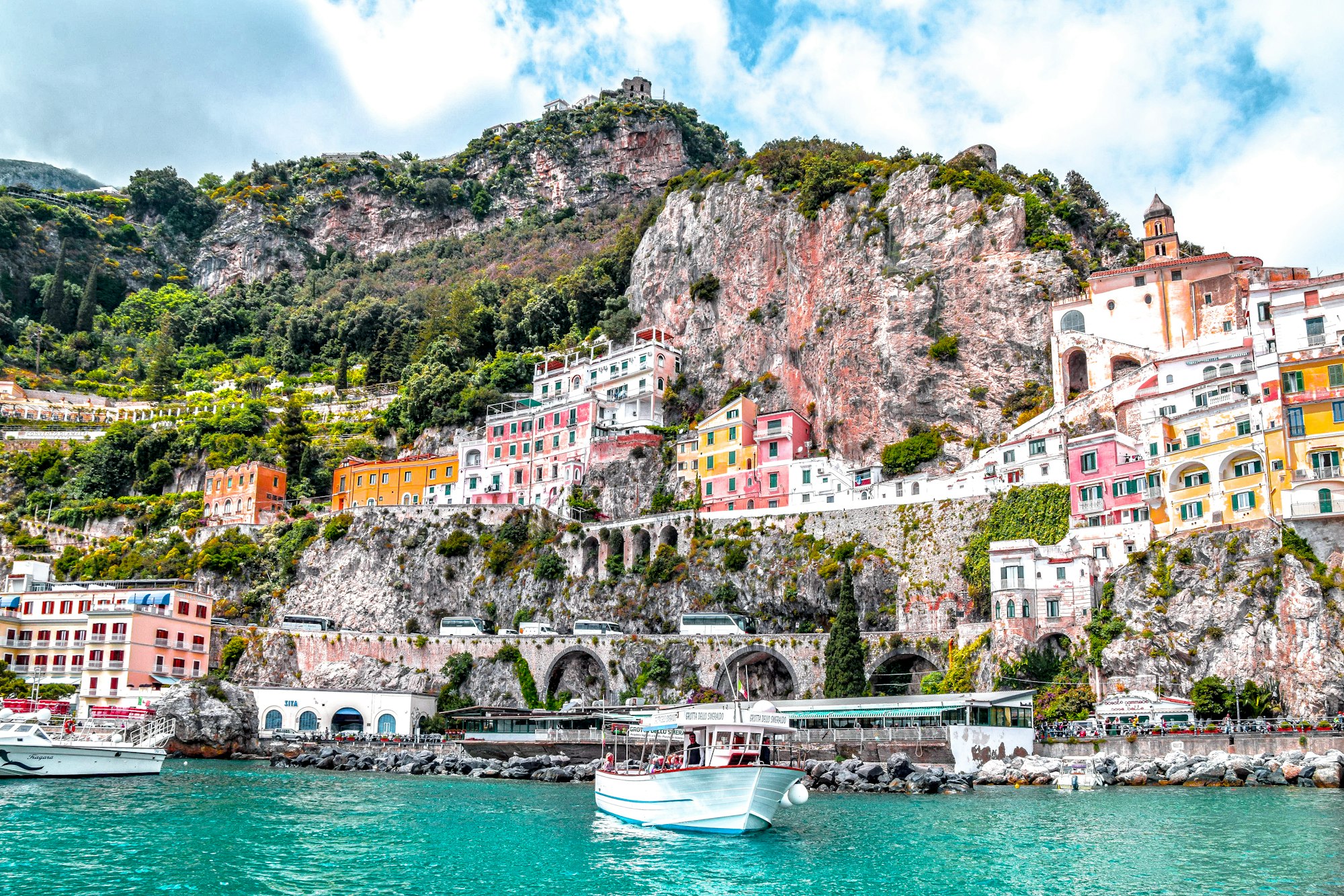 A pastel cliffside town of the Amalfi Coast seen from the water, small boats on a blue sea