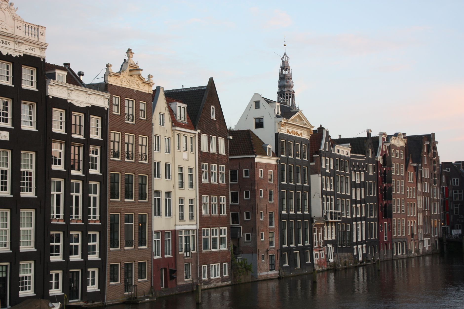 A tree-lined Amsterdam canal at dusk, arched bridge, houseboats and reflections on the water