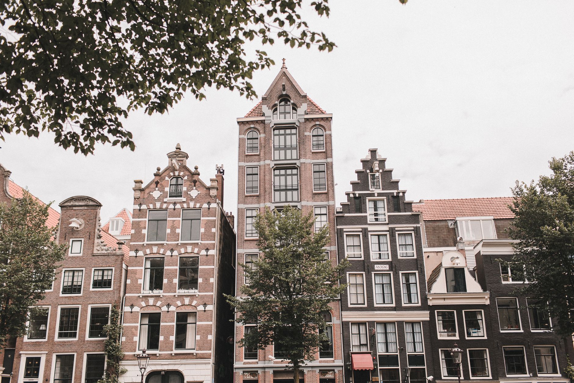 Tall narrow Amsterdam canal houses with stepped and bell gables, several leaning forward slightly