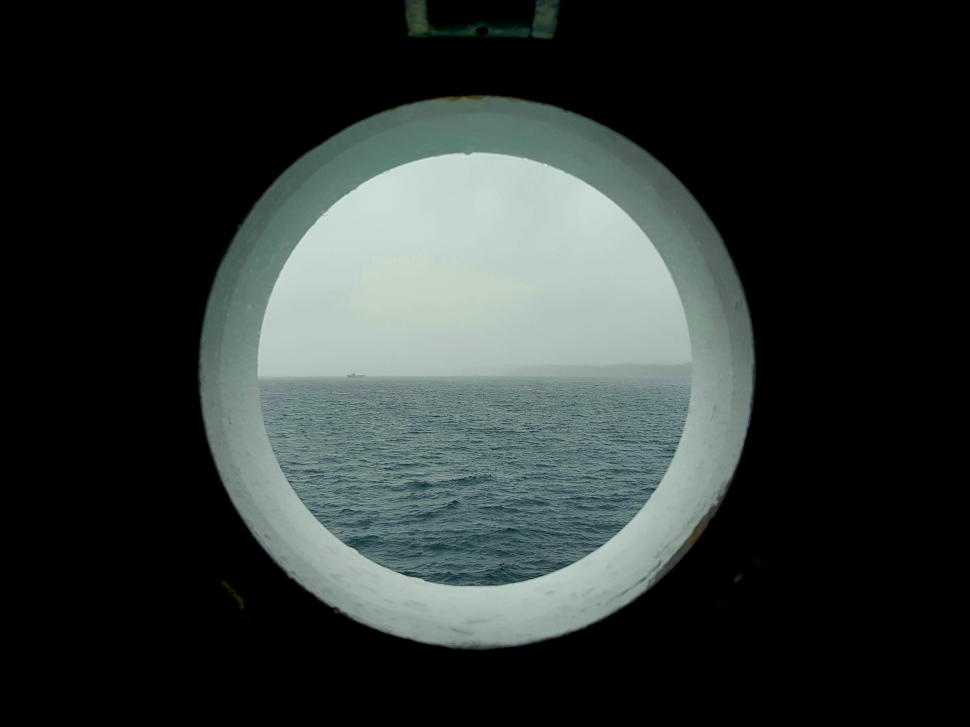 Grey sea and a pale sky framed in a round ship's porthole