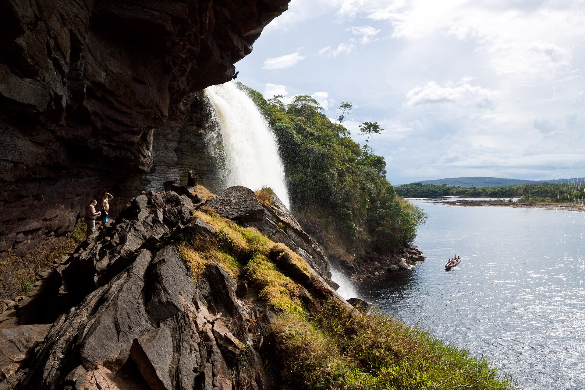 A waterfall spilling over dark rock into the wide brown lagoon at Canaima with forest and islands beyond