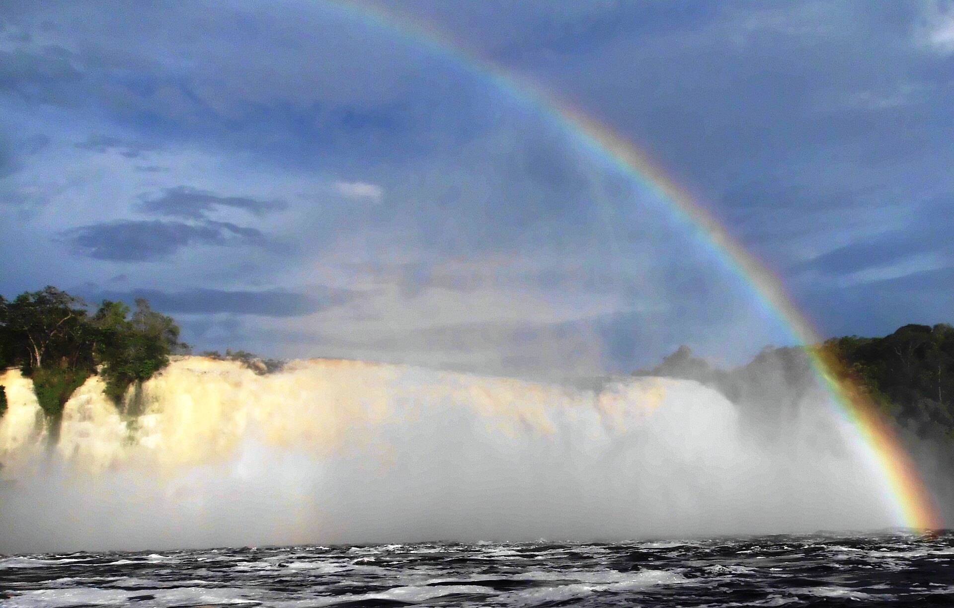 A broad waterfall crashing into the Canaima lagoon with a full rainbow arching through the spray