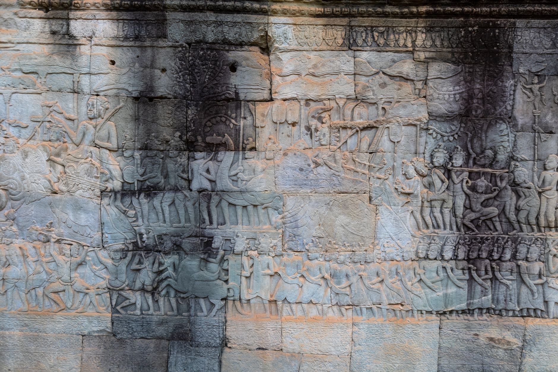 A long sandstone gallery wall at Angkor Wat carved with rows of figures in bas-relief