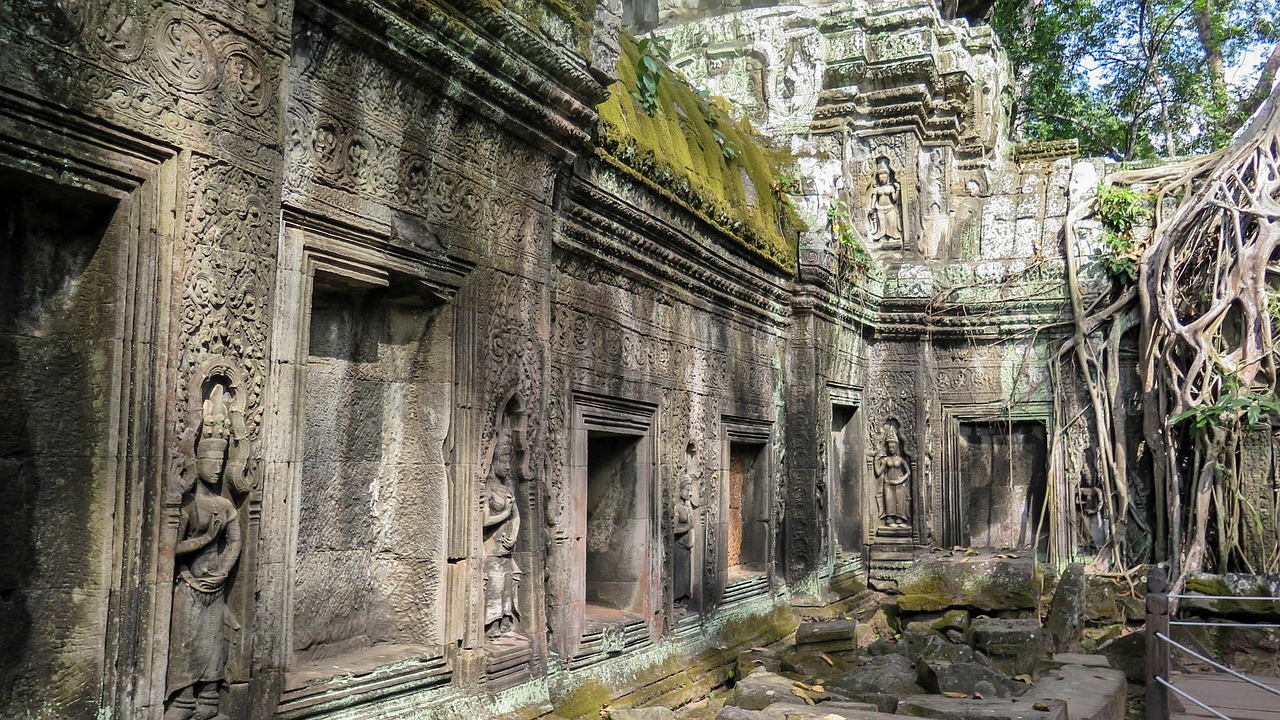 Pale roots of a strangler fig pouring over the stone wall of a temple gallery at Ta Prohm