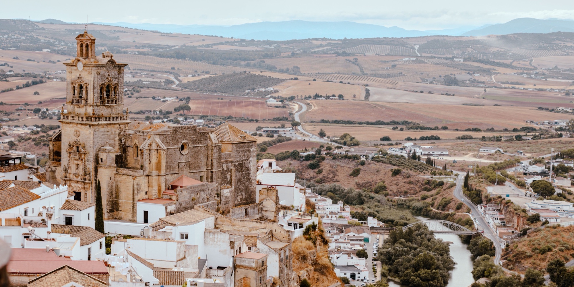 The church of San Pedro at the edge of the cliff in Arcos de la Frontera, with white houses below and the Guadalete river and farmland beyond