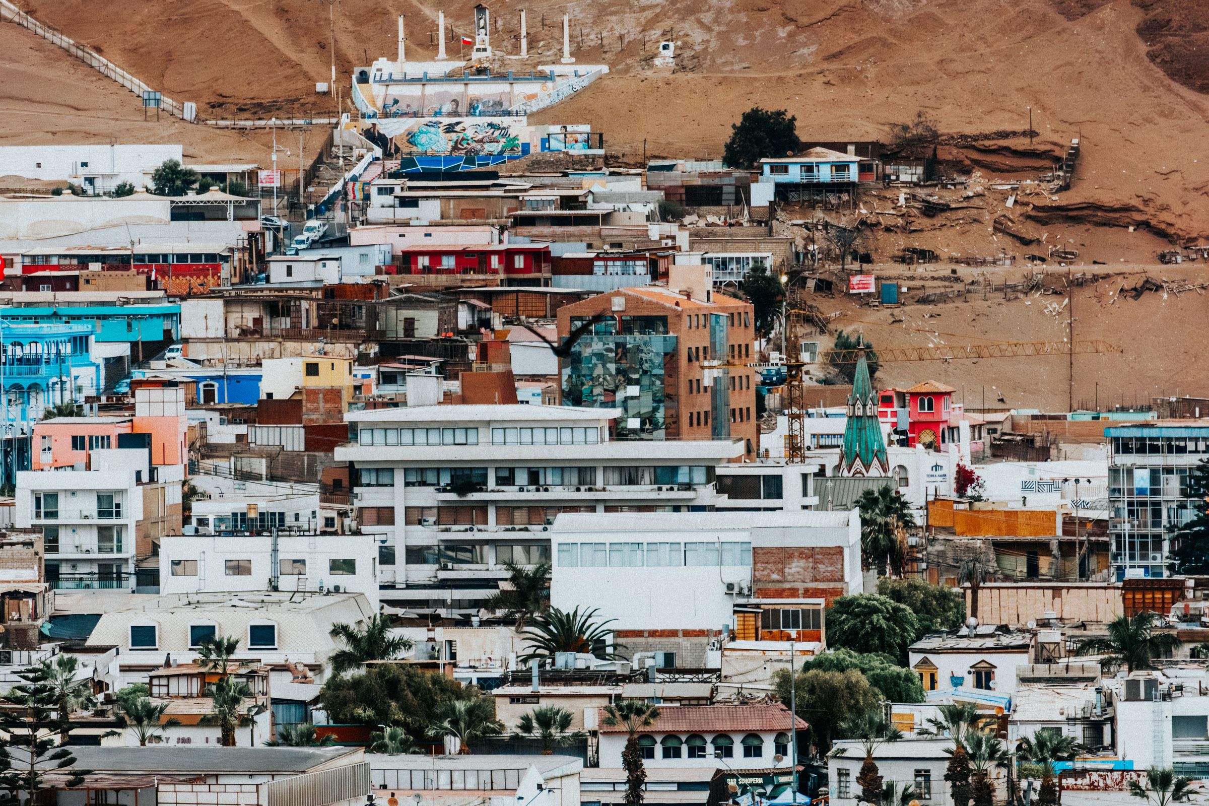 Brightly painted houses climbing a dry hillside in Arica, with bare desert slopes rising behind them