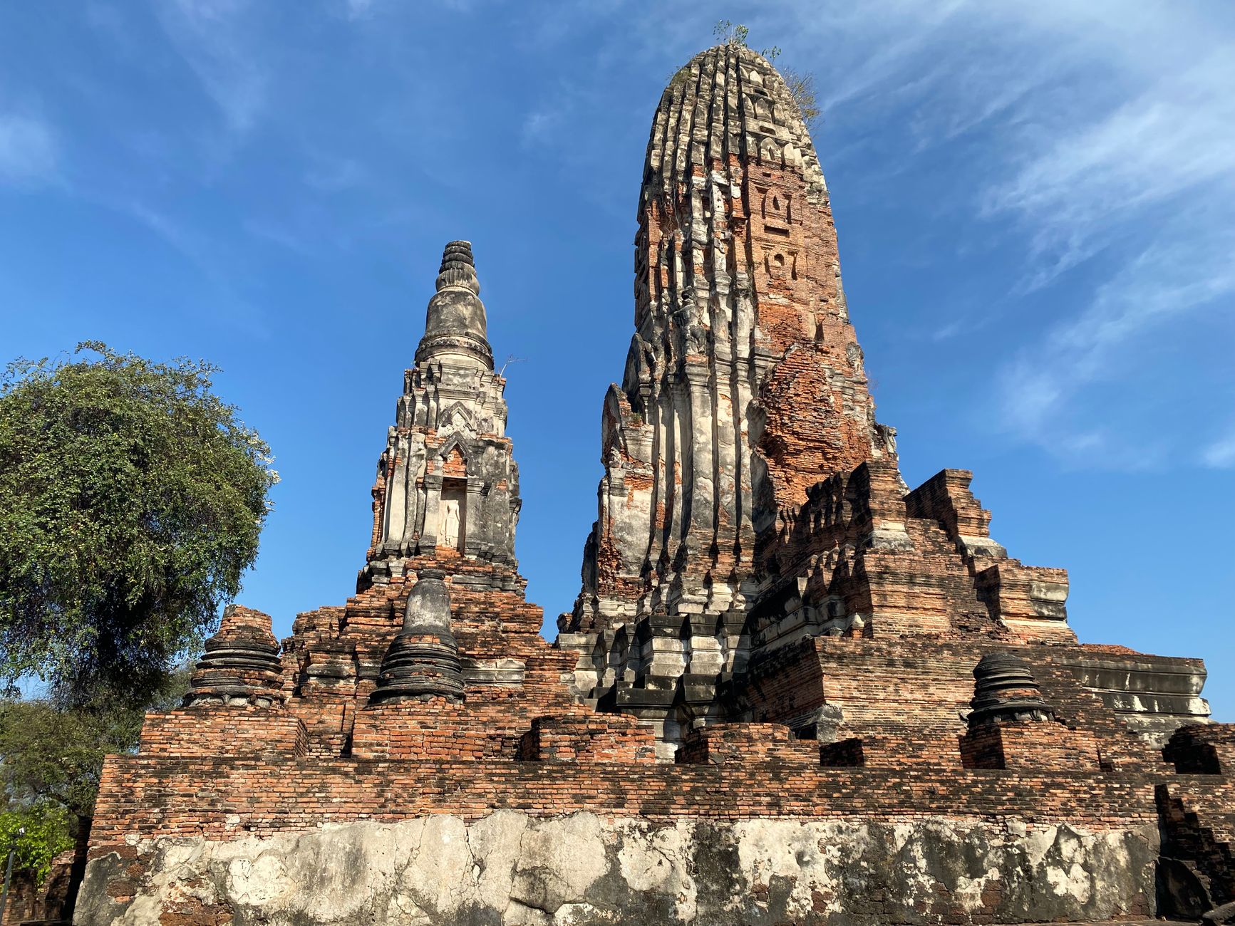 Two tall Khmer-form prangs of different sizes on a shared brick platform against a blue sky, with small stub chedis along the platform edge