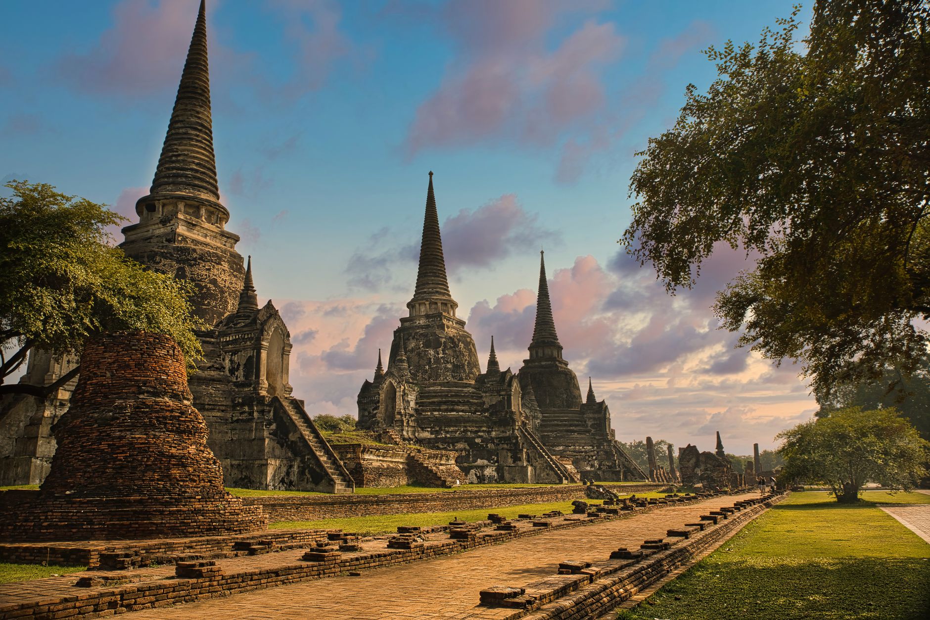 Three restored bell-shaped chedis in a row at Wat Phra Si Sanphet with a processional avenue running towards them in low sun
