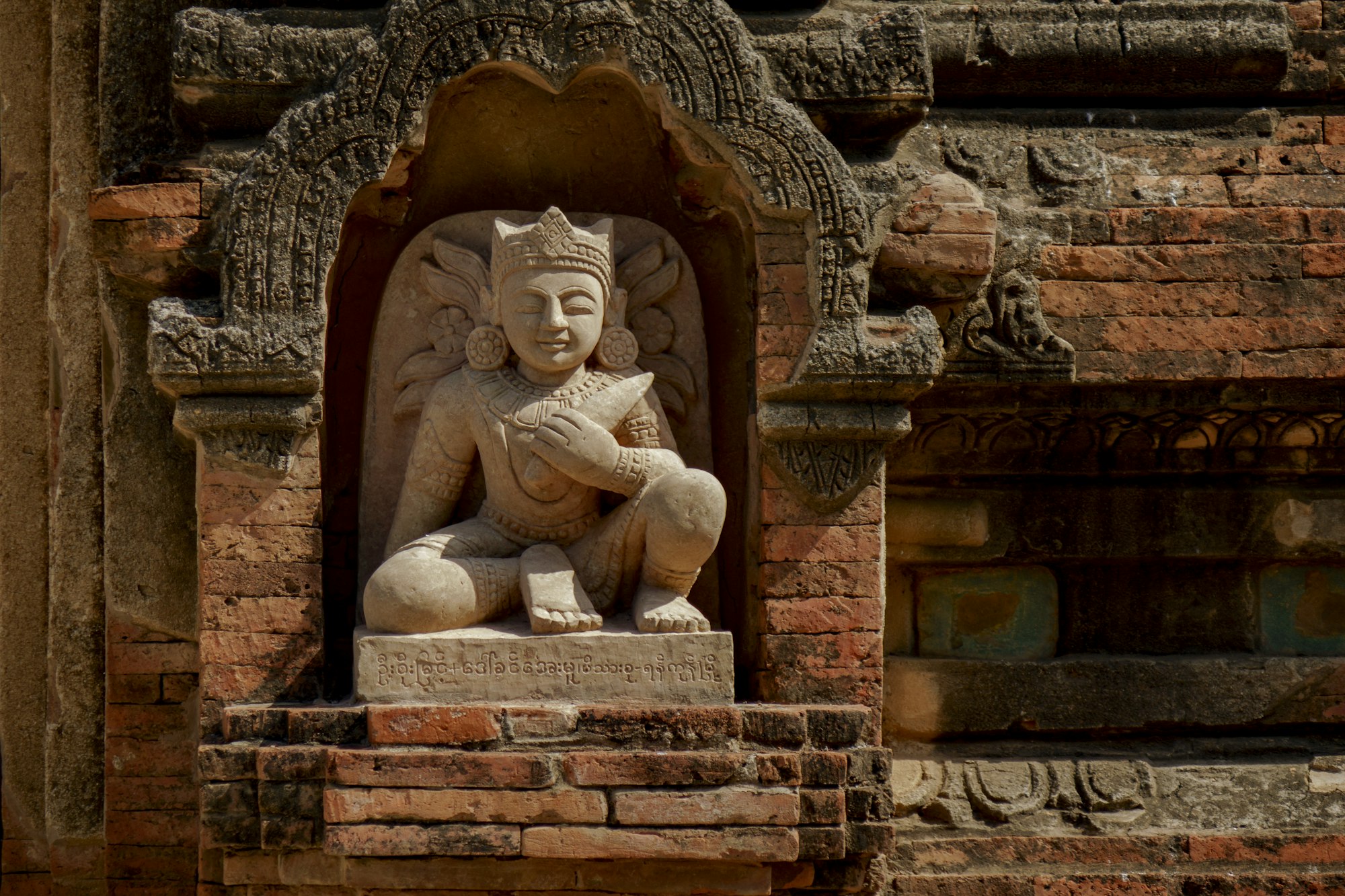 A carved seated Buddha in a niche inside a brick Bagan temple