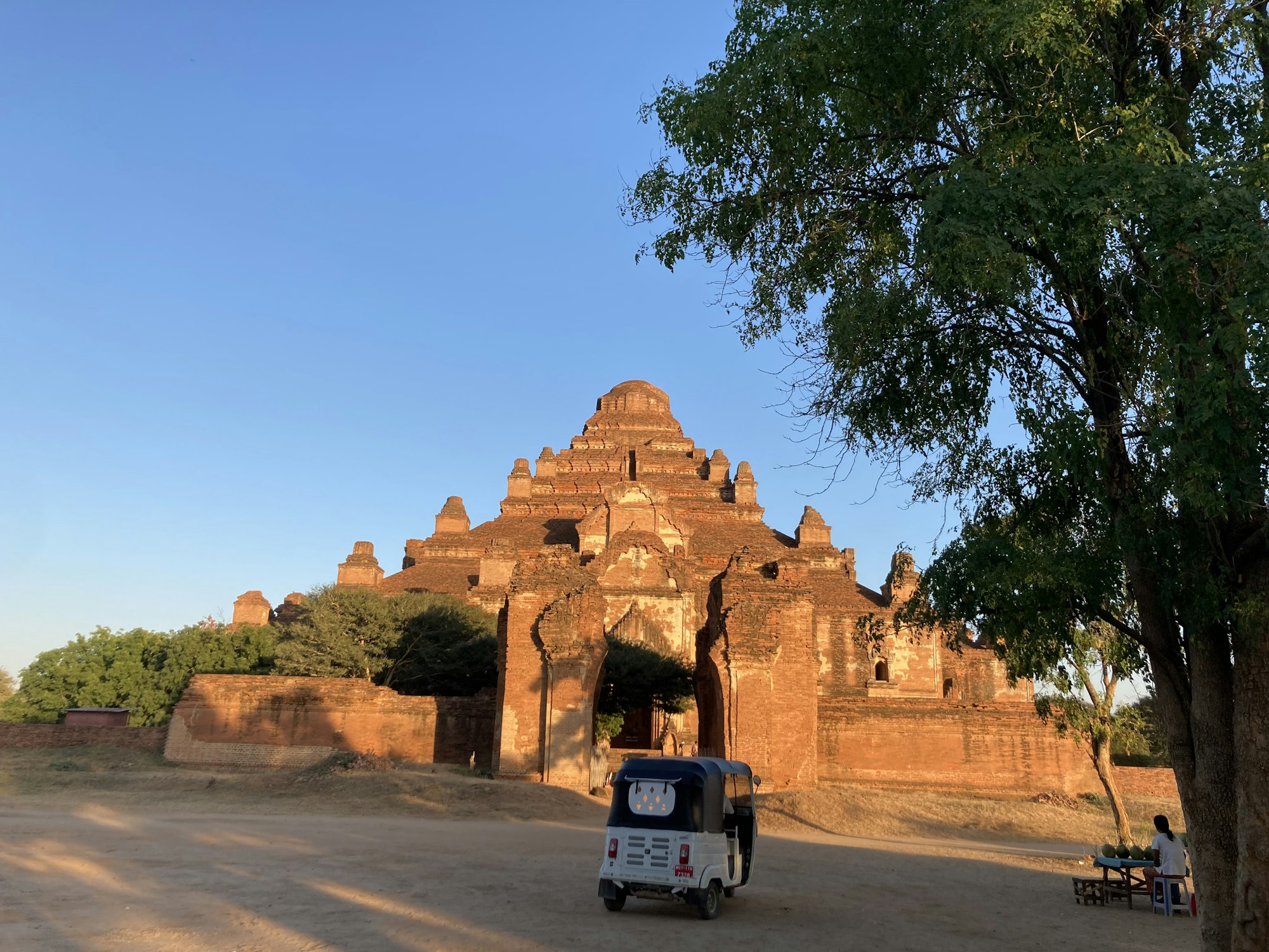 The massive red-brick pyramid mass of Dhammayangyi temple in evening light, a tuk-tuk parked before it