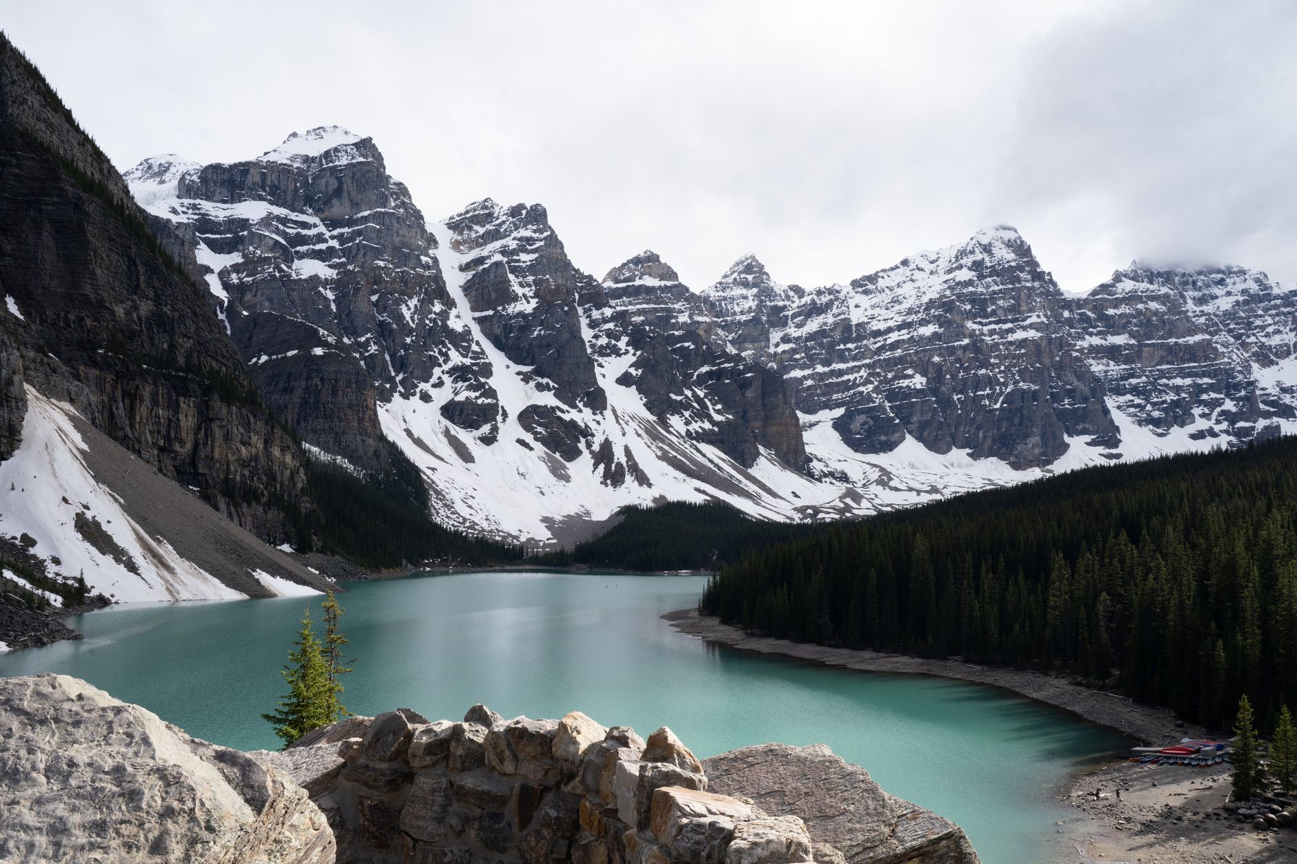 Moraine Lake's turquoise water below the snow-streaked Valley of the Ten Peaks with boulders in the foreground