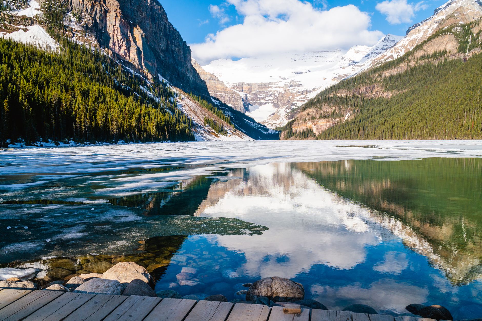 Lake Louise at spring break-up, patches of ice on still water below the Victoria Glacier