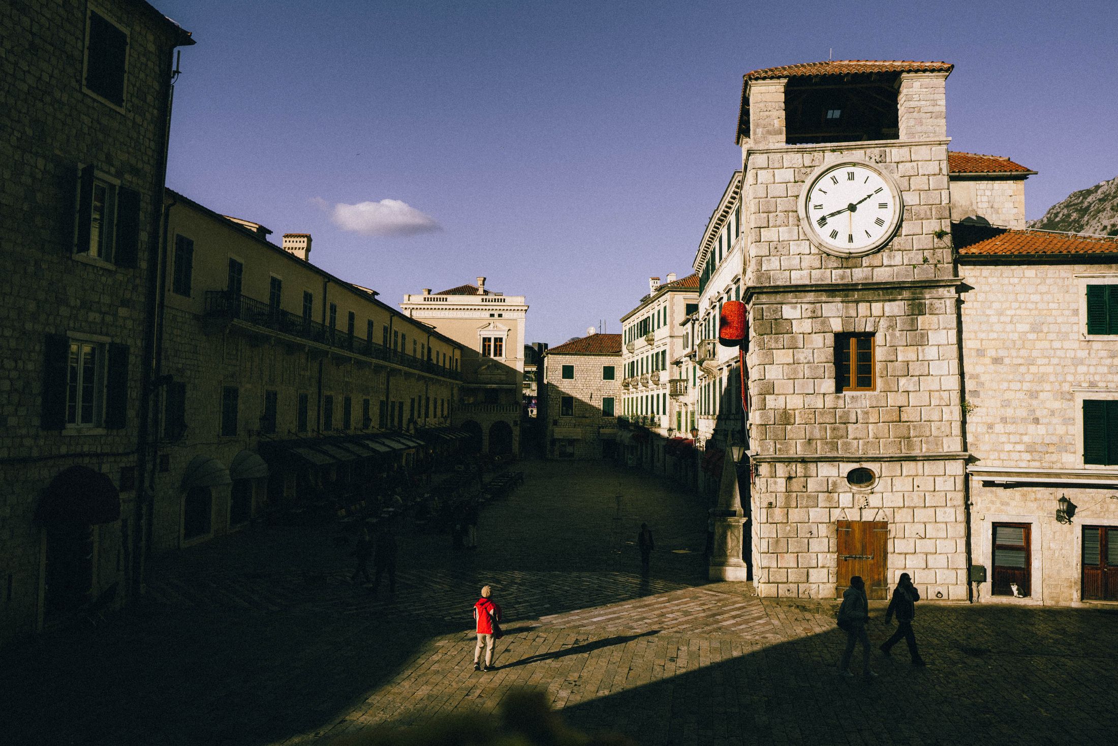 A sunlit square in Kotor old town with the medieval clock tower and Venetian stone buildings