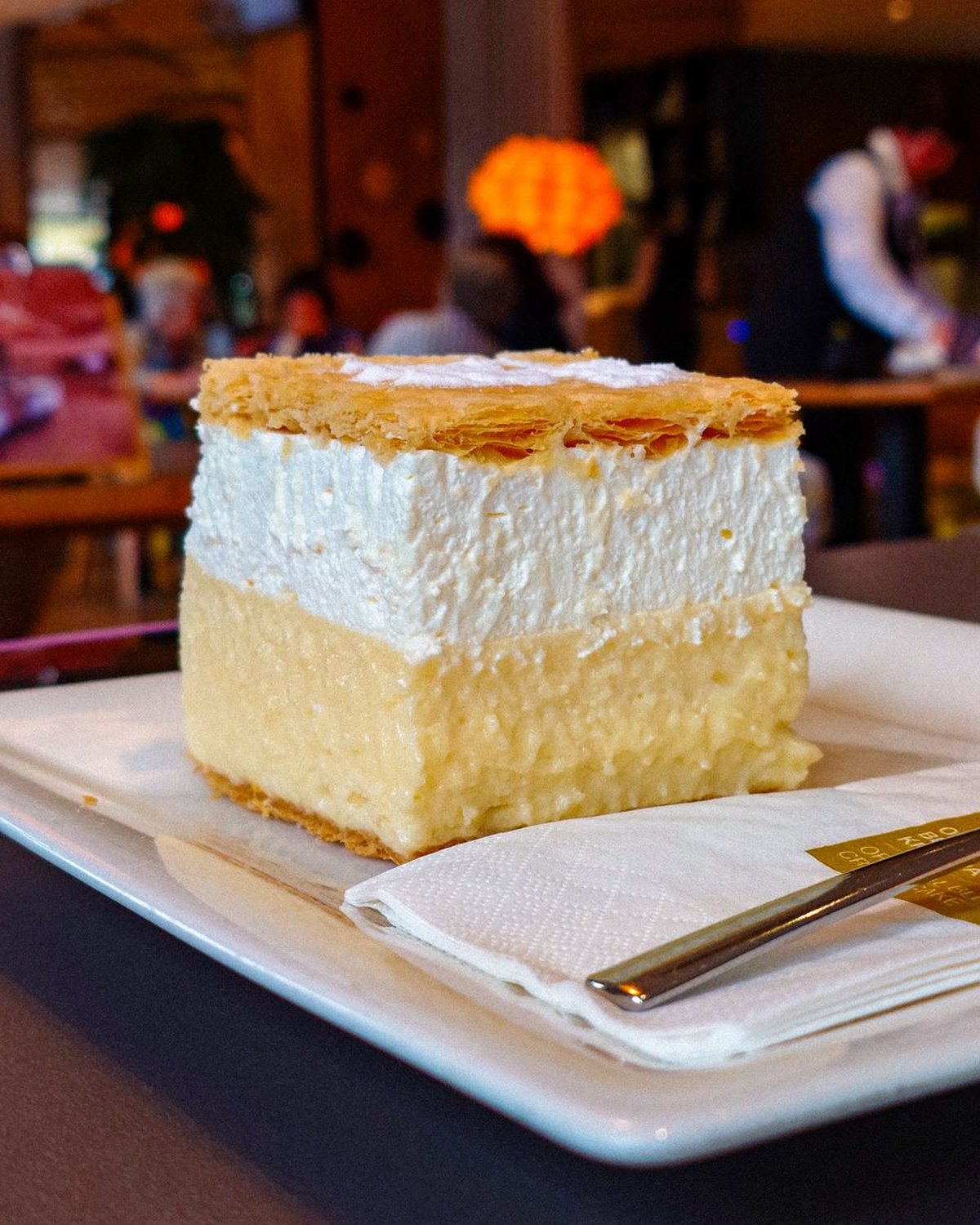 A slice of kremsnita, the Bled cream cake, custard and whipped cream between layers of puff pastry dusted with sugar, on a plate in a cafe