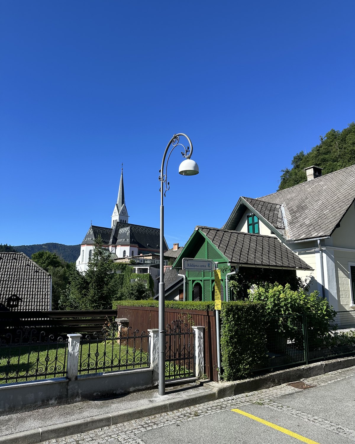 A street in the town of Bled away from the lake, an ornate green kiosk and a church spire under a blue sky