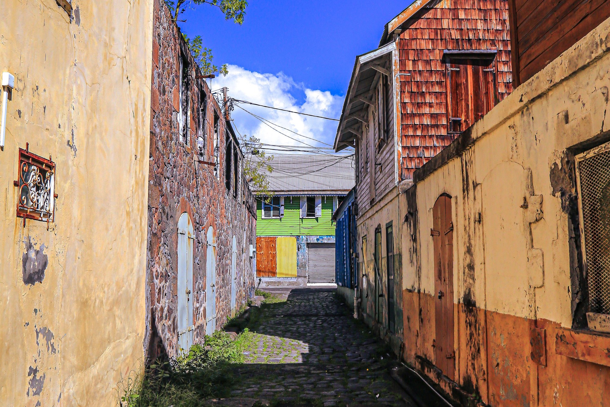 A narrow lane in Roseau between a stone wall and painted wooden buildings