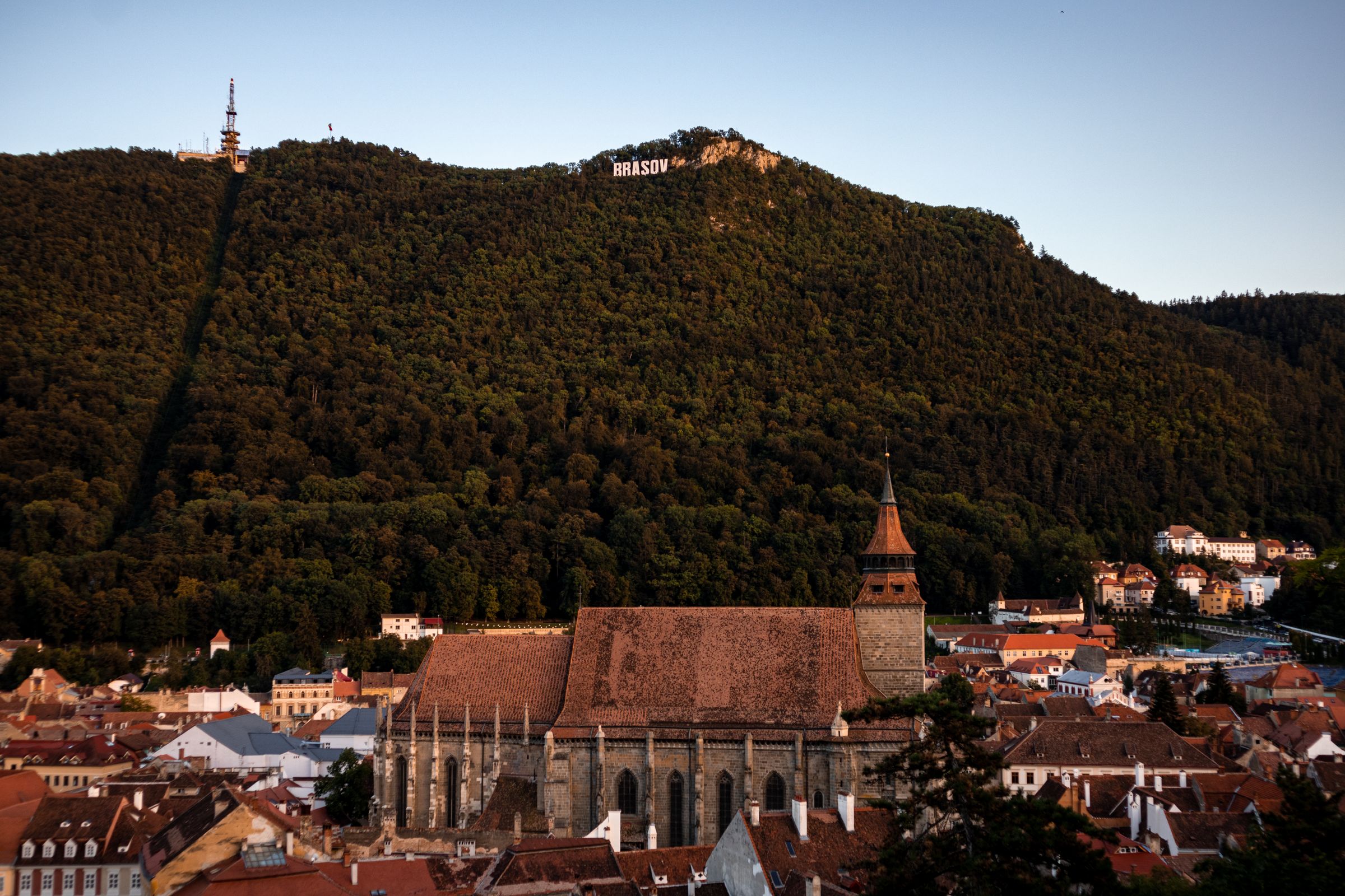 The Black Church's long roof and tower above the old town of Brașov, with the forested slope of Tâmpa behind and the town's name in white letters near the summit