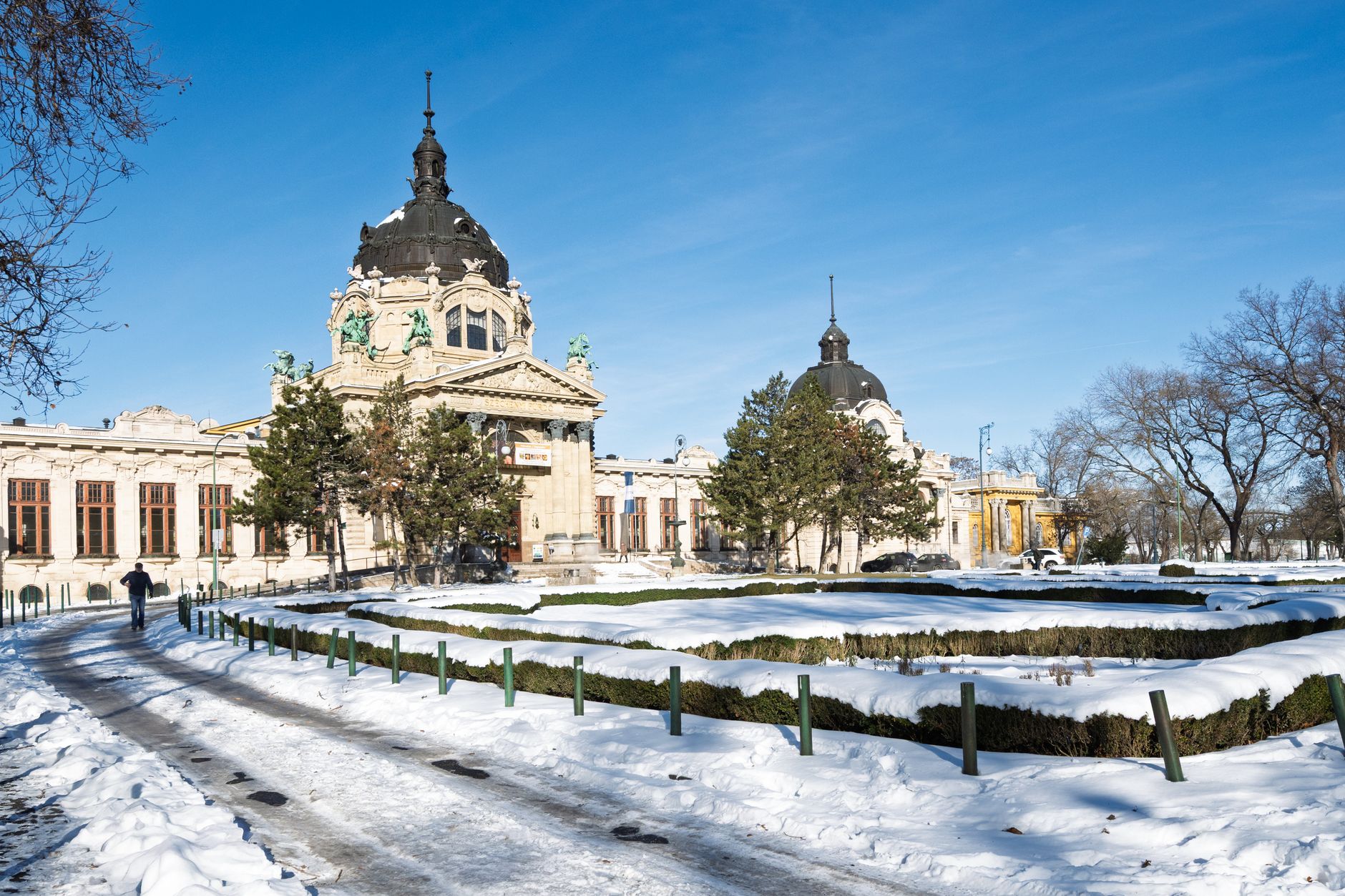 The snow-covered Szechenyi bath building and its clipped gardens under a clear winter sky