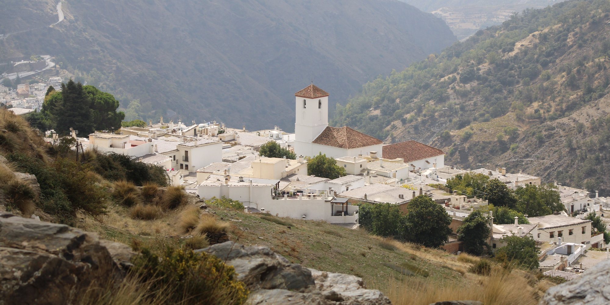 Capileira's white houses and church tower on a slope of the Poqueira gorge, with the valley falling away to the south between dry mountain sides