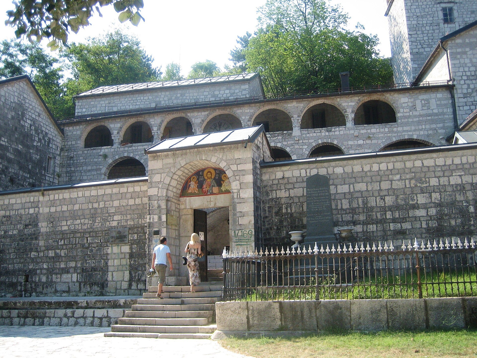 The stone arcaded front of Cetinje Monastery above a flight of steps, with visitors at the entrance