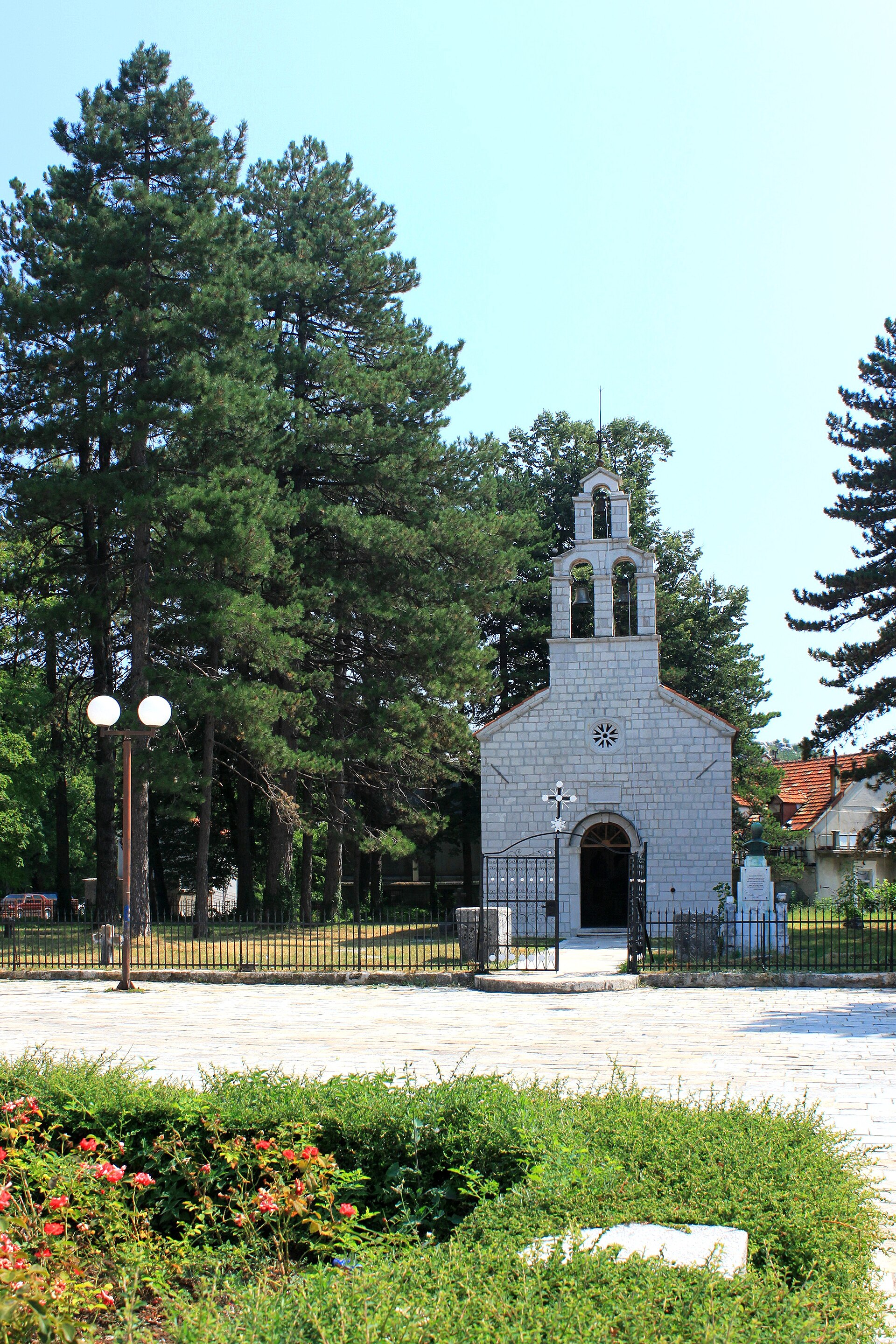 The Vlaška crkva in Cetinje, a small white stone church with a triple bellcote, standing behind a low iron railing among tall pines