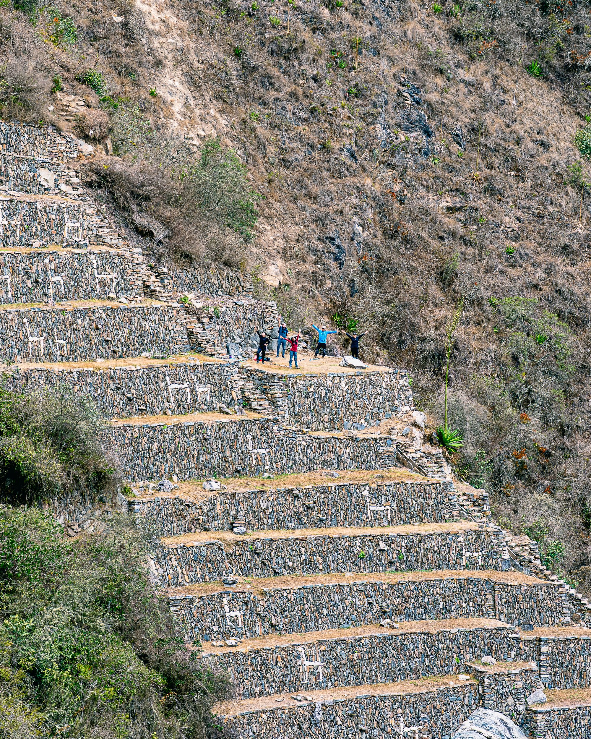 The white-stone llama terraces of Choquequirao, tiny trekkers standing on the steps for scale
