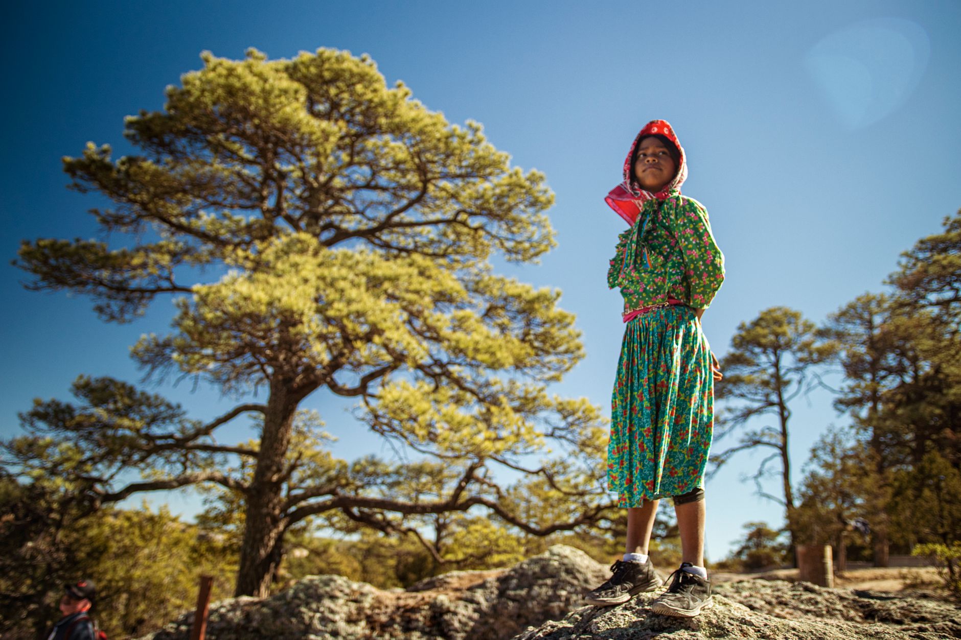 A Raramuri girl in traditional dress on a rock in the Sierra Tarahumara