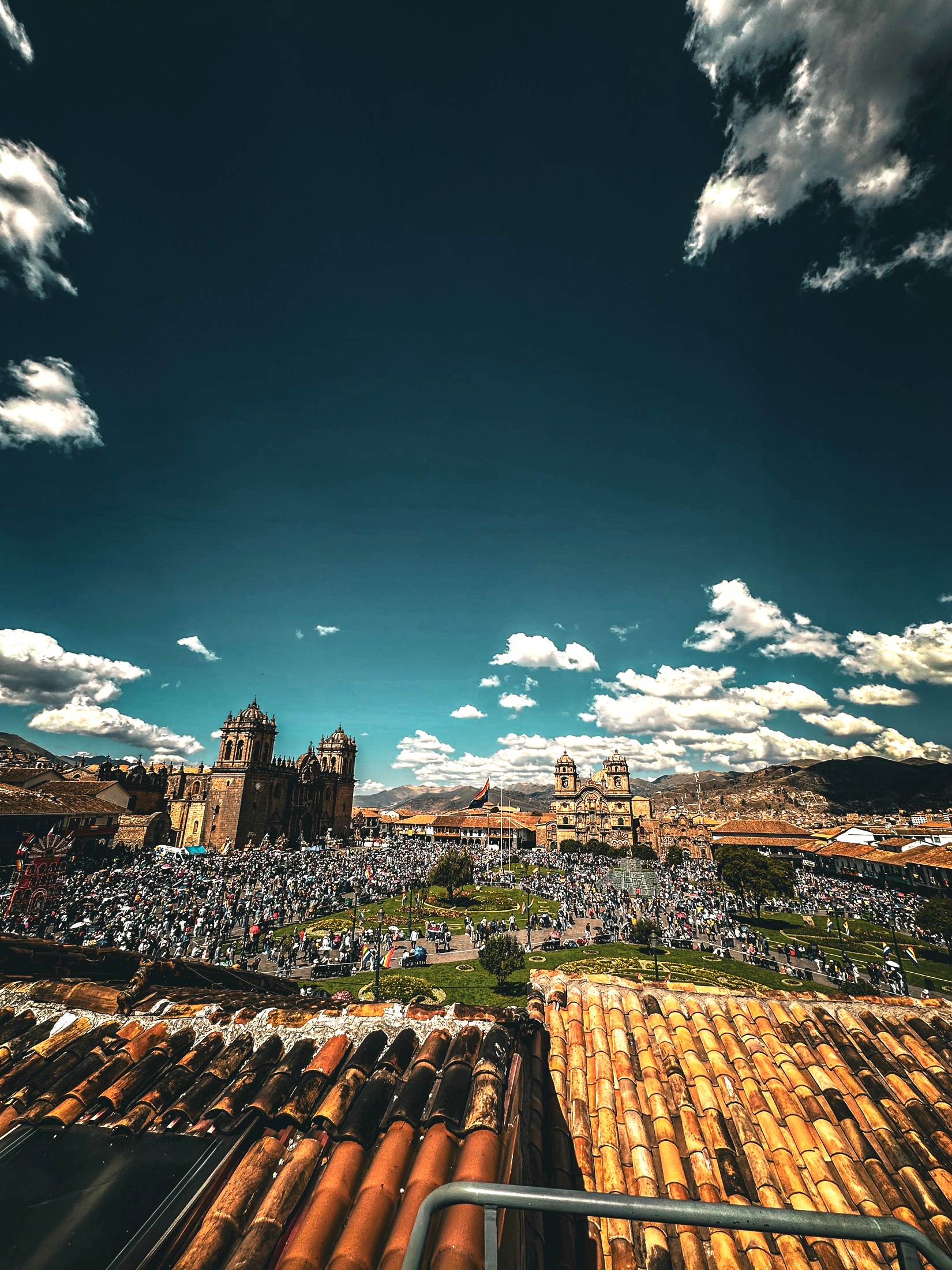 The Plaza de Armas of Cusco seen from a tiled rooftop, filling with crowds, the cathedral and La Compañía church across the square