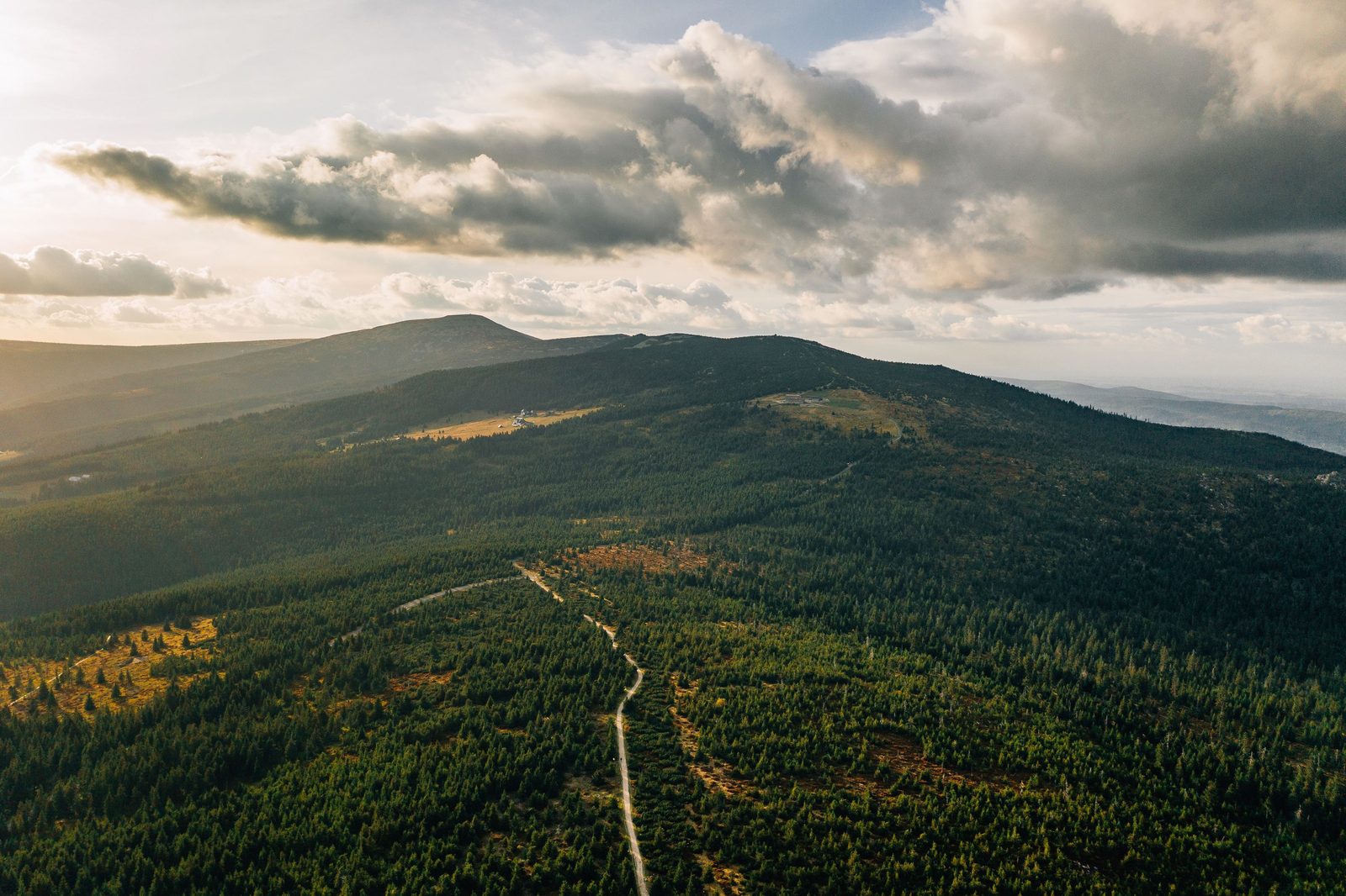 A forested Krkonoše ridge seen from the air above Špindlerův Mlýn, a trail running along it under a cloudy sky