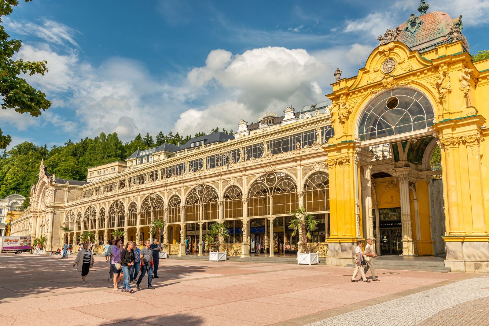 The yellow cast-iron spa colonnade at Mariánské Lázně, its arcade running along a paved square under a blue sky