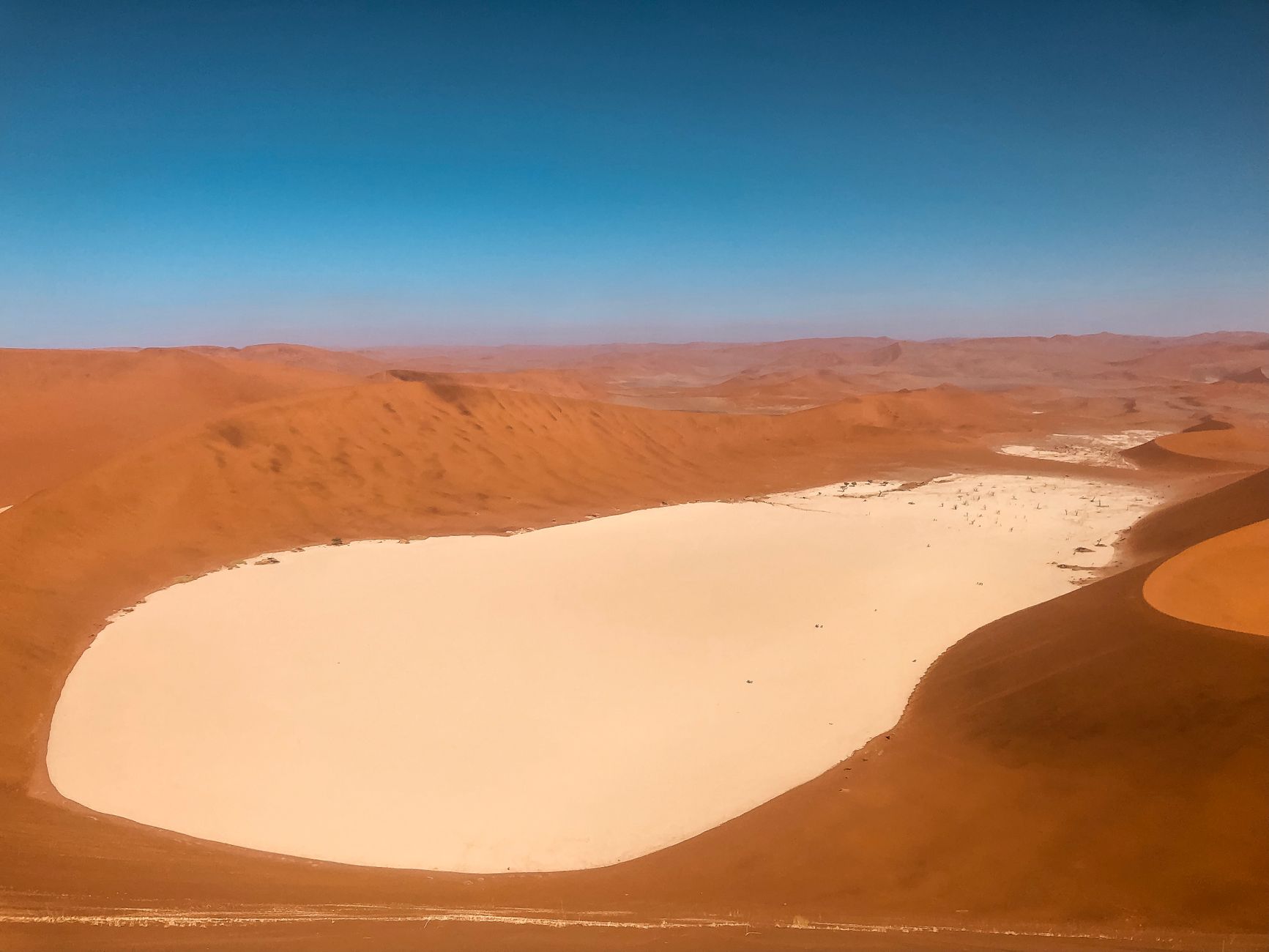 Aerial view of a pale clay pan enclosed by enormous red dunes in the Namib Sand Sea