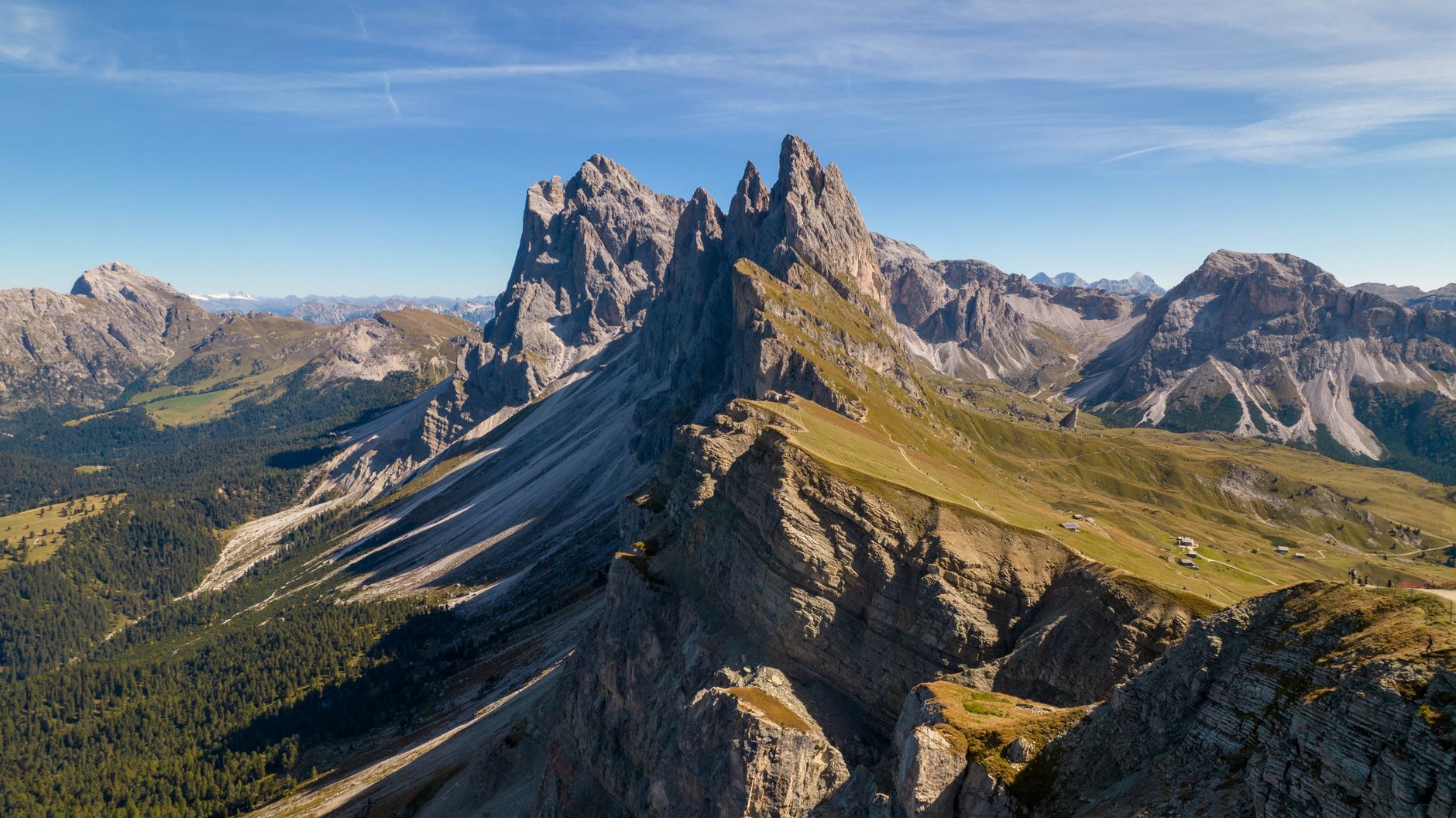 Serrated Dolomite ridge rising from green alpine meadow under blue sky
