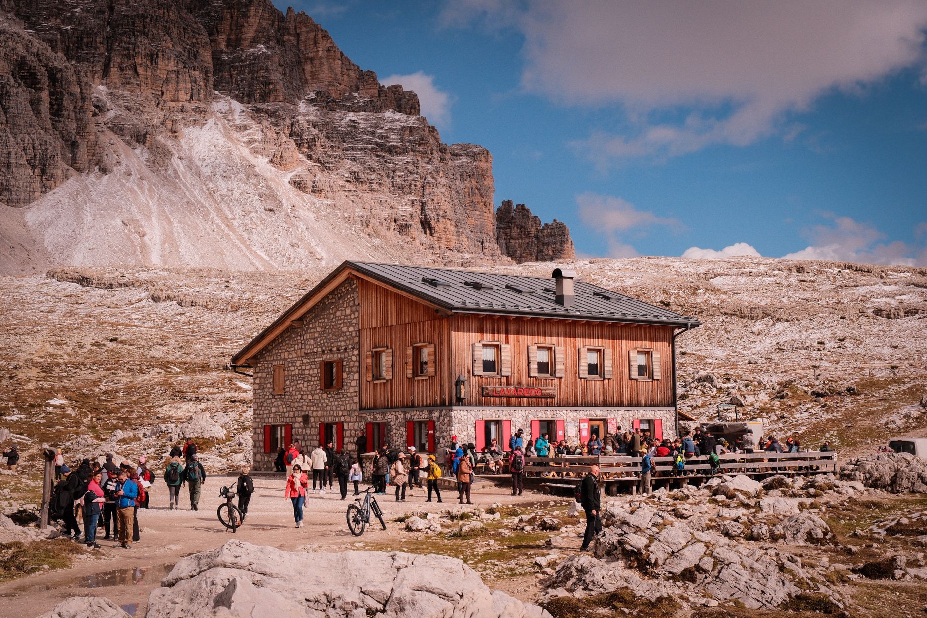 Stone and timber mountain refuge with a busy terrace under a pale rock wall