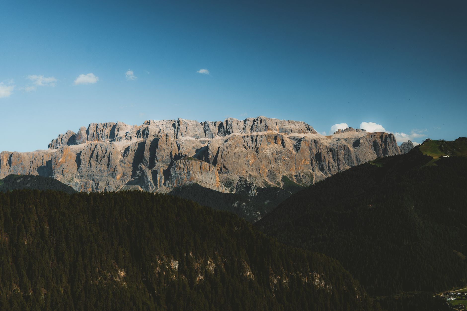 Flat-topped Sella massif with vertical pale walls above a forested ridge