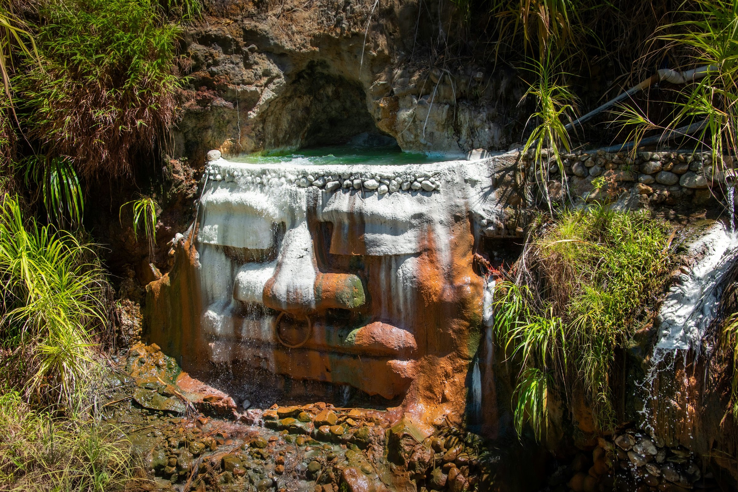 Terraced hot spring pools with white mineral crust and orange staining on the rock beside them at Titou Gorge