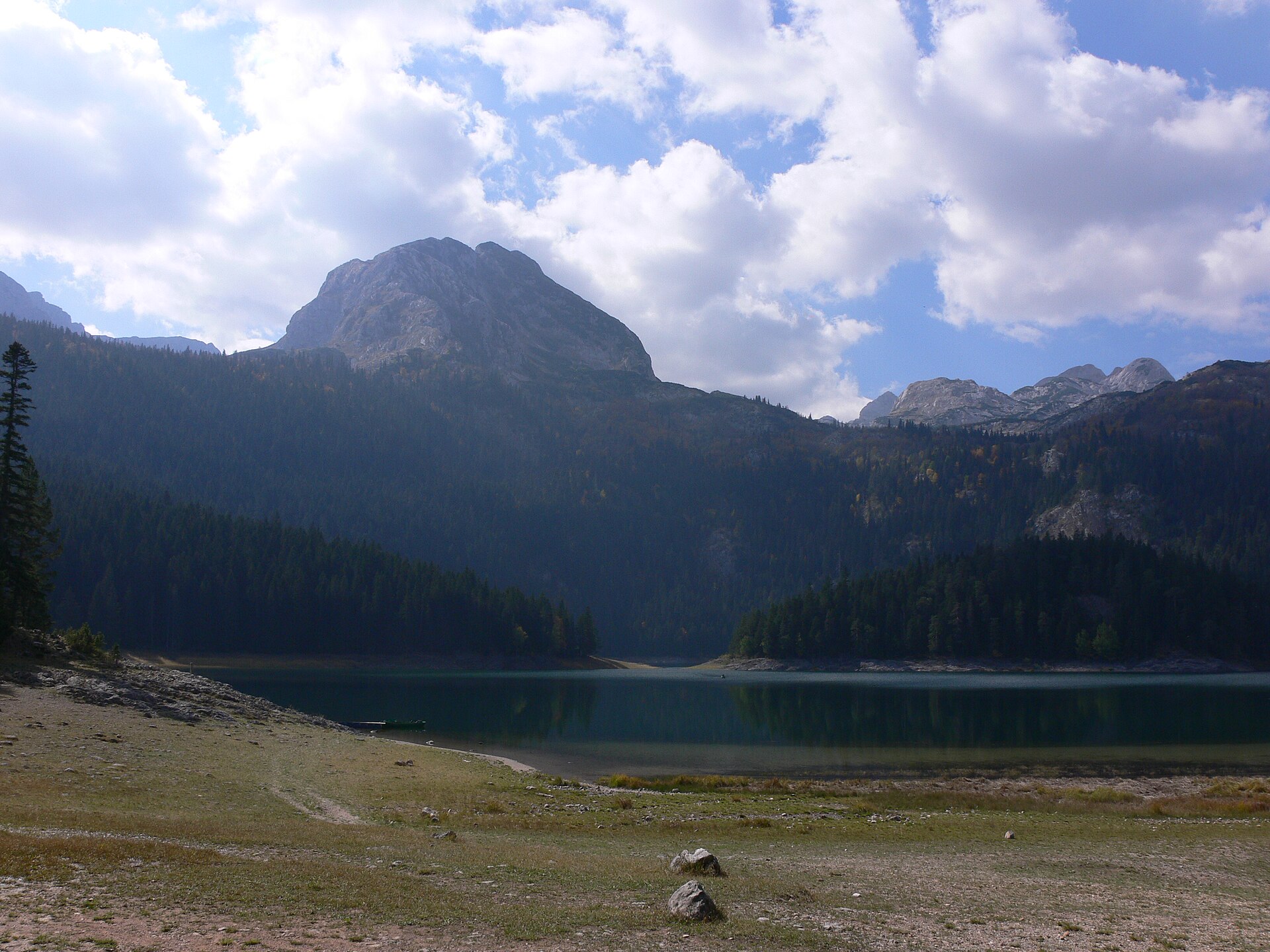 The rock summit of Meded rising above the dark water of Black Lake at Durmitor, conifer forest along the shore