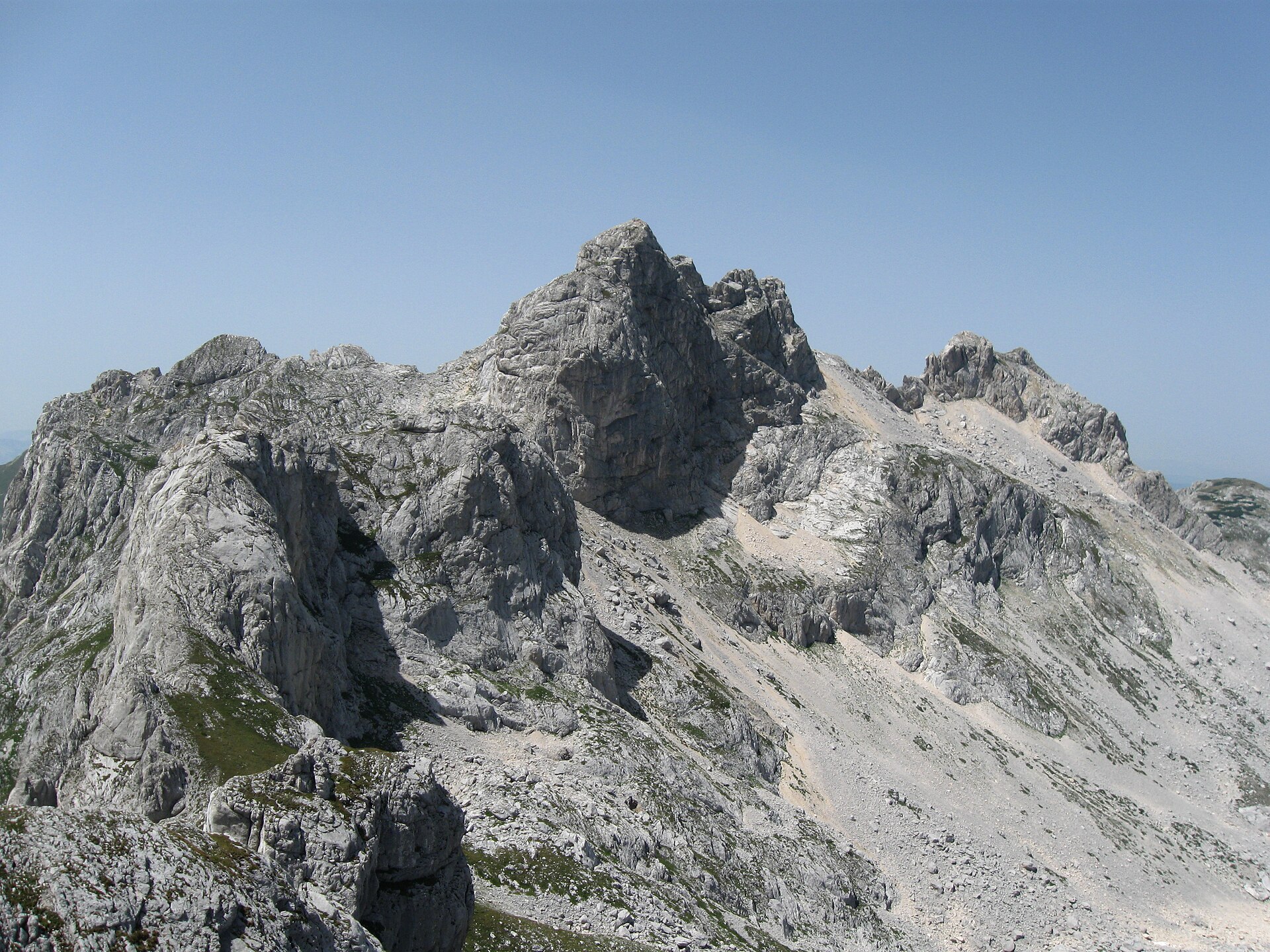 The grey rock summit of Bobotov Kuk at Durmitor seen from a neighbouring ridge under a blue sky