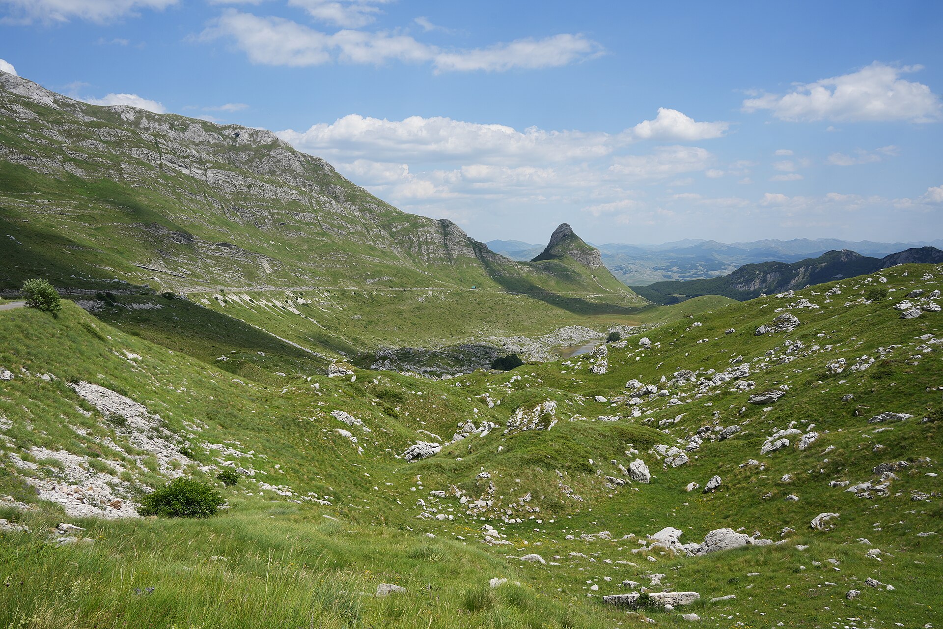 The green valley at the Sedlo pass in Durmitor with the conical peak of Stožina and rocky slopes beyond