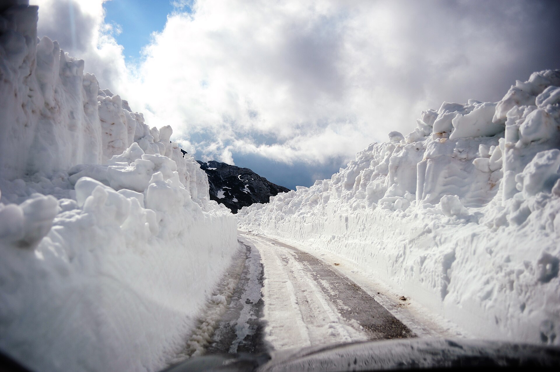 A road at Durmitor cut through snow banks standing higher than a car on both sides