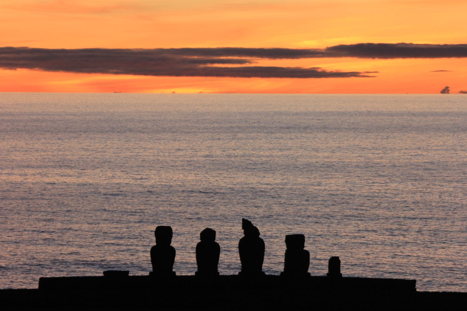 Five moai silhouetted on a platform above the Pacific against an orange sunset