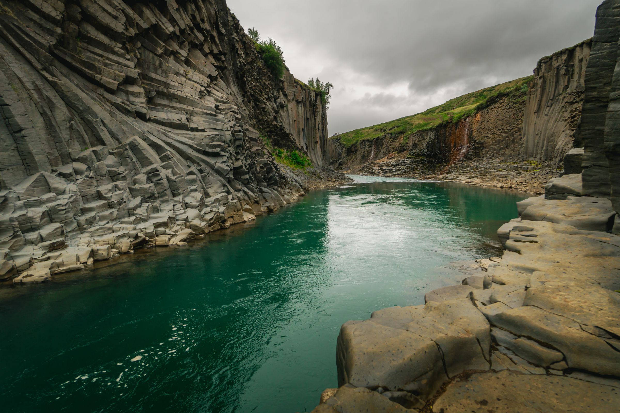 Basalt columns rising on both walls of the Stuðlagil canyon, with a turquoise river running between them
