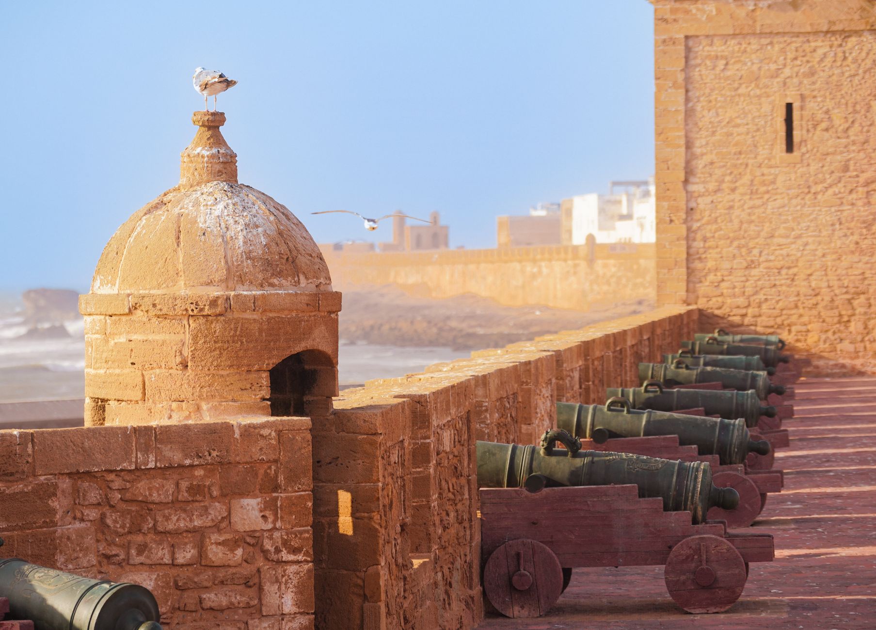 A row of old cannons along the stone sea wall of the Skala de la Ville, a domed turret at its corner and the Atlantic beyond