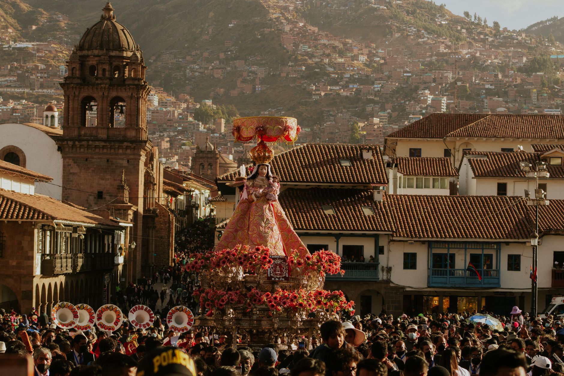 An image of the Virgin on a flower-banked litter carried through the crowd on the Plaza de Armas of Cusco at Corpus Christi, the tower of La Compañía behind