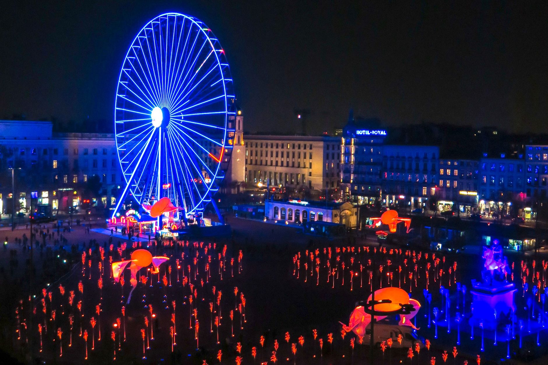 Place Bellecour in Lyon during the Fête des Lumières, filled with red light stems beside a blue-lit Ferris wheel