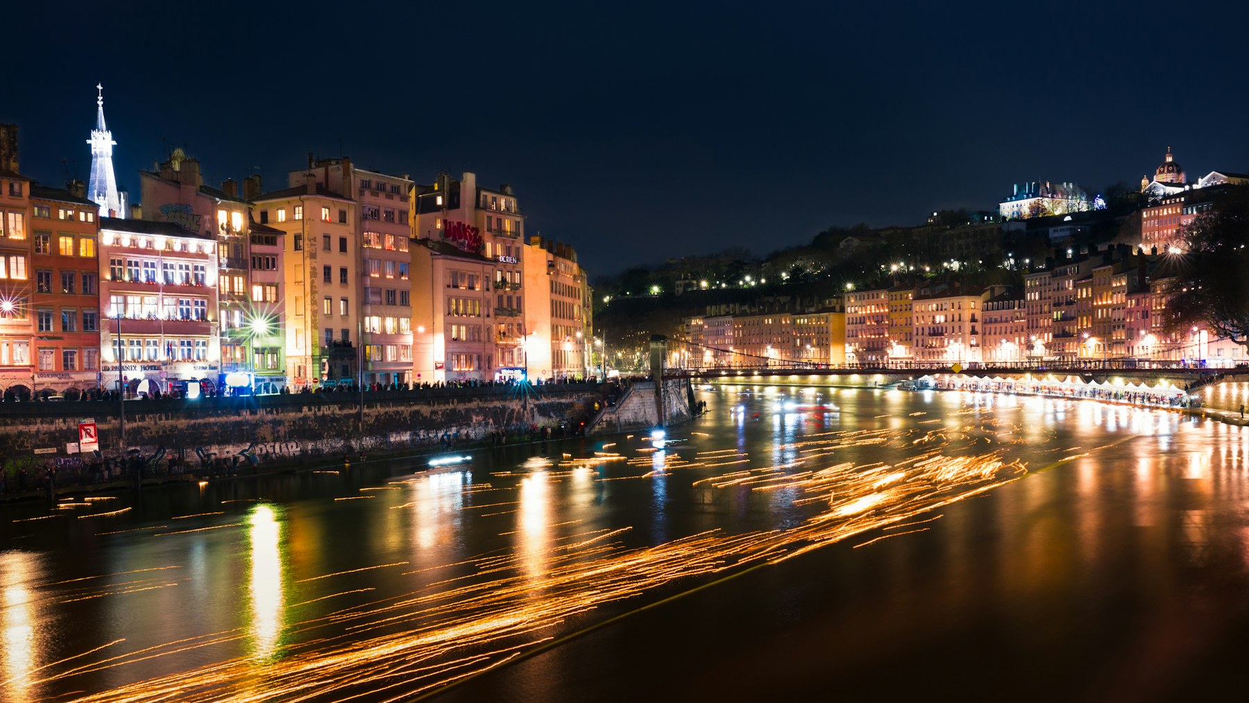 Candles floating on the Saône at night below the lit houses of Vieux Lyon during the Fête des Lumières