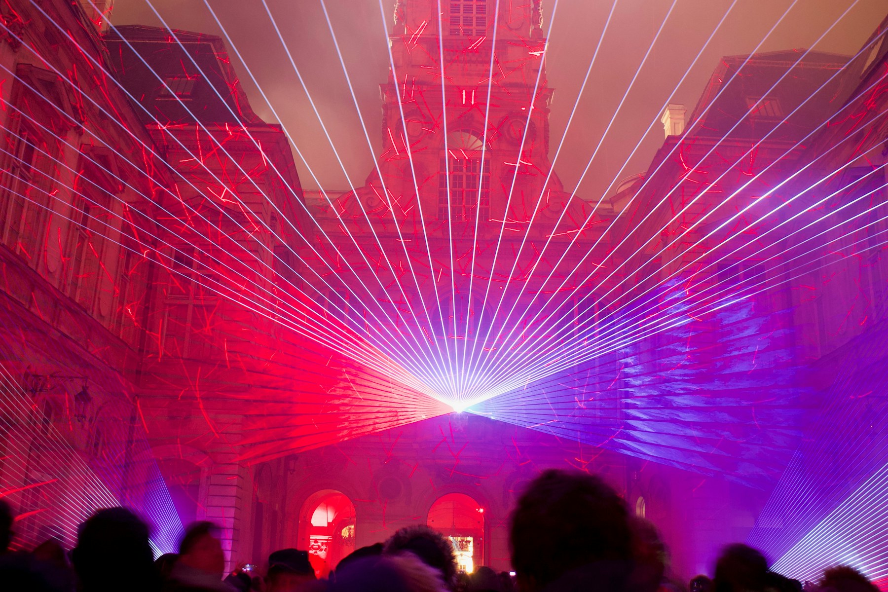 Lasers in red and violet across the Hôtel de Ville of Lyon, with a crowd in silhouette, during the Fête des Lumières