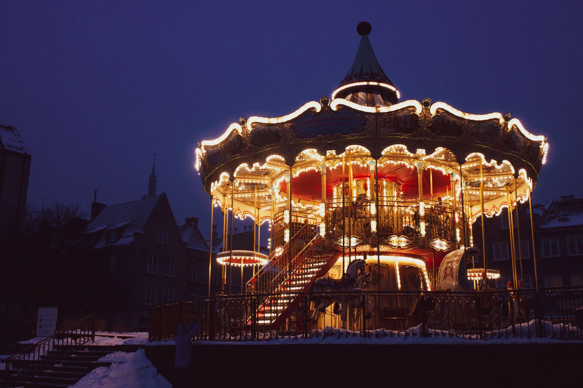 A lit double-decker carousel in falling snow at night in Gdańsk
