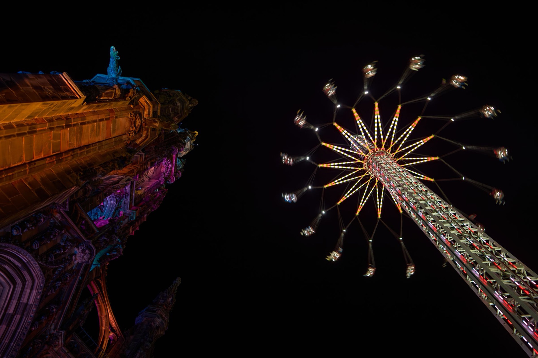 The Scott Monument lit in colour at night beside a fairground swing ride in Princes Street Gardens, Edinburgh, in the winter festival season